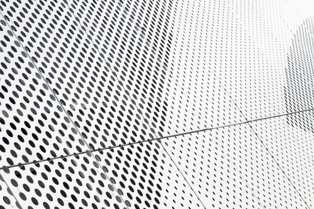 Diagonal view of metall grilles and round holes in metal surface, perforated panels close-up.